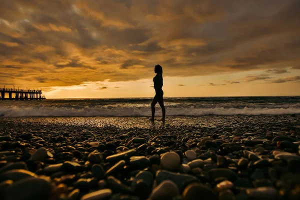 Silueta de mujer joven en la playa del atardecer — Foto de Stock