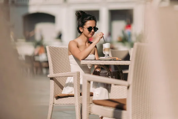 Mujer atractiva en gafas de sol y vestido sentado en un café y beber café — Foto de Stock