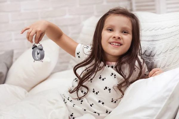 little child girl in pyjamas with clock