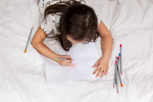 Niña haciendo dibujos mientras está acostada en la cama . —  Fotos de Stock