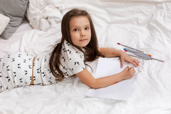 Mała dziewczynka rysunek Zdjęcia leżąc na łóżku. — Zdjęcie stockowe