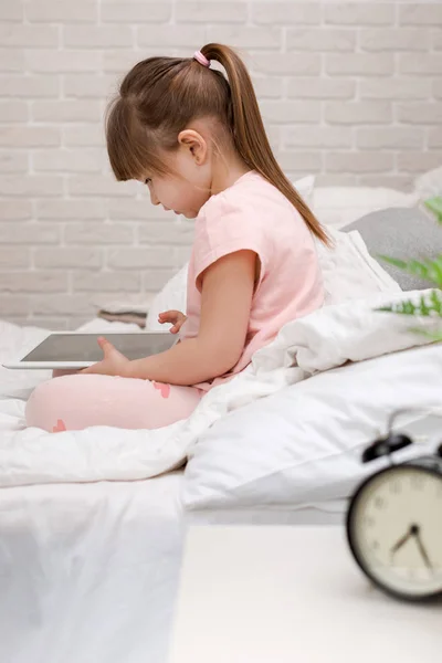 Menina minúscula mente na cama usa tablet digital. — Fotografia de Stock