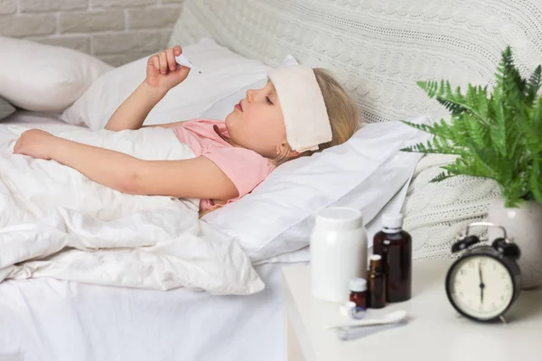 Hasta küçük küçük kız termometre ile yatakta yatan. — Stok fotoğraf