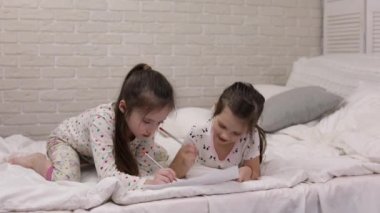 çocuklar yatakta yatarken resim çizer.