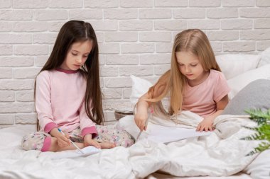 çocuklar yatakta yatarken resim çizer.