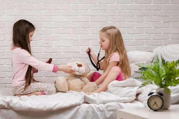 Двоє милих дівчаток, які грають у лікаря з плюшевим ведмедем — стокове фото