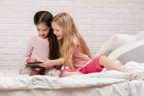 Két aranyos gyerekek lányok használata digitális tabletta az ágyban. — Stock Fotó