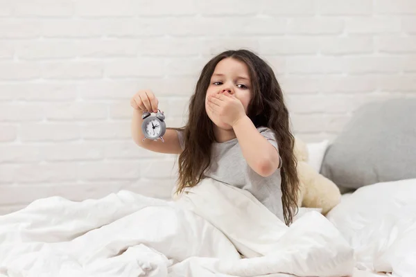 Little girl in pyjamas with clock — Stock Photo, Image