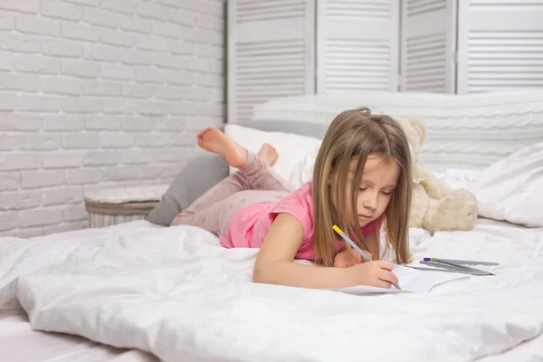 Bonito menina desenho imagens enquanto deitado na cama — Fotografia de Stock