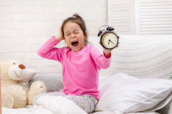 Little girl in pyjamas with clock — Stock Photo, Image