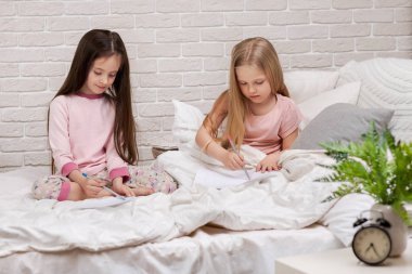 çocuklar yatakta yatarken resim çizer.