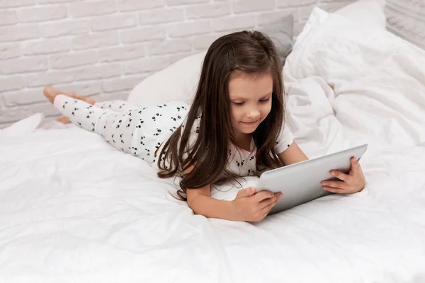 Malá holčička leží v posteli používá digitální tablet. — Stock fotografie