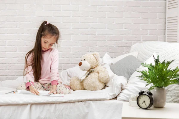 Маленька дівчинка малює фотографії, лежачи на ліжку . — стокове фото
