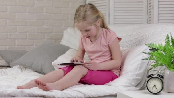 Cute little child girl lies in bed uses digital tablet. — Stock Video