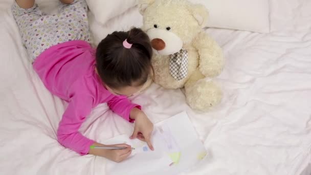 Bonito menina desenho imagens enquanto deitado na cama . — Vídeo de Stock