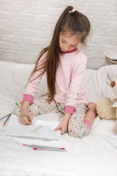 Liten flicka ritning bilder medan liggande på sängen. — Stockfoto