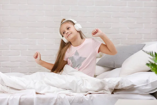 Küçük kız yatakta kulaklıklar ile müzik dinlerken. — Stok fotoğraf