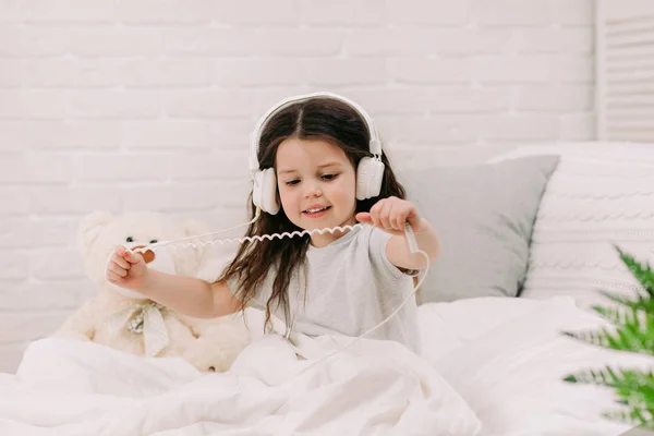 Mała dziewczynka słucha muzyki ze słuchawkami na łóżku. — Zdjęcie stockowe