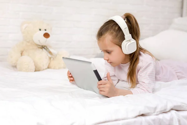 Schattig klein meisje ligt in bed maakt gebruik van digitale Tablet. — Stockfoto