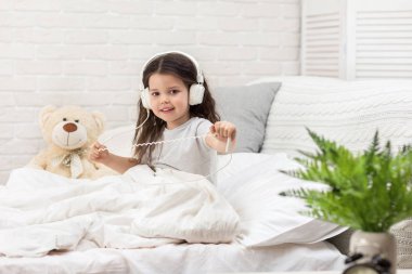 küçük kız yatakta kulaklıklar ile müzik dinlerken.