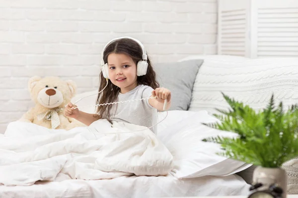침대에 헤드폰으로 음악을 듣고 어린 소녀. — 스톡 사진