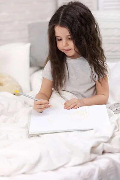 Schattig klein meisje tekening Foto's terwijl liggend op bed — Stockfoto