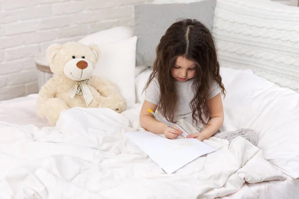 Niedliches kleines Mädchen, das Bilder zeichnet, während es auf dem Bett liegt — Stockfoto