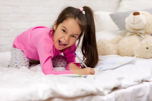 Bonito menina desenho imagens enquanto deitado na cama — Fotografia de Stock