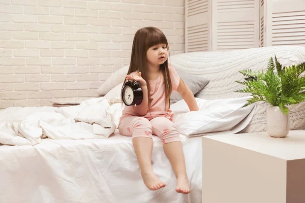 little child girl in pyjamas with clock