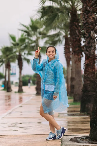 young woman tourist in raincoat smiling and looking at the camera under rain