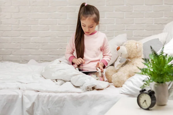 Liten barn flicka ligger i sängen Använder Digital tablett. — Stockfoto