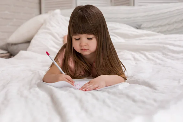 Menina desenho fotos enquanto deitado na cama . — Fotografia de Stock