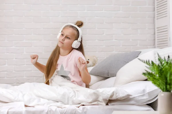 Niña escuchando la música con los auriculares en la cama . — Foto de Stock