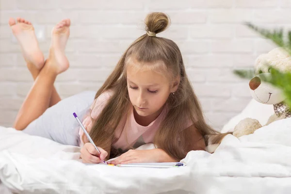 Χαριτωμένο μικρό κορίτσι σχεδιάζοντας φωτογραφίες, ενώ ξαπλωμένο στο κρεβάτι — Φωτογραφία Αρχείου
