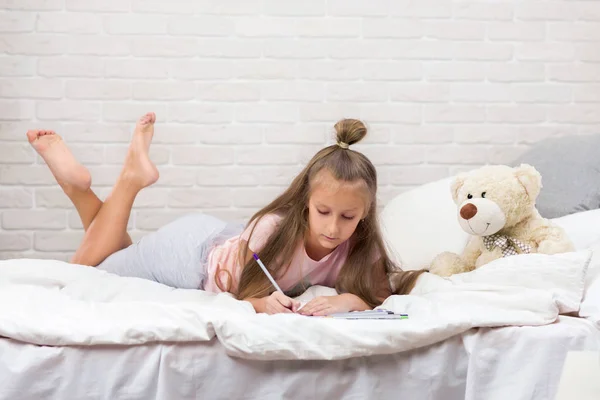 Bonito menina desenho imagens enquanto deitado na cama — Fotografia de Stock