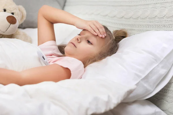 Sick little girl lying in bed with thermometer — Stock Photo, Image