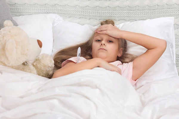 Sick little girl lying in bed with thermometer — Stock Photo, Image