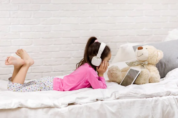 Cute Little Girl leży w łóżku używa cyfrowego tabletu. — Zdjęcie stockowe
