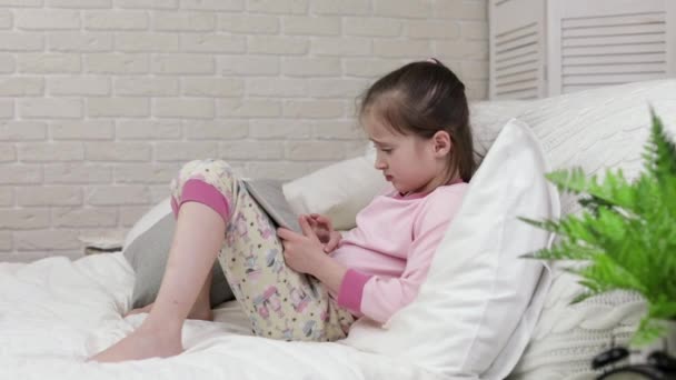 Cute little child girl lies in bed uses digital tablet. — Stock Video