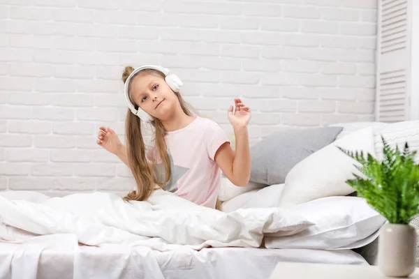 Маленька дівчинка слухає музику з навушниками на ліжку . — стокове фото