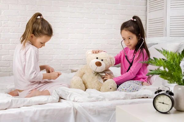 Zwei süße Kinder Mädchen spielen Arzt mit Teddybär zu Hause. — Stockfoto