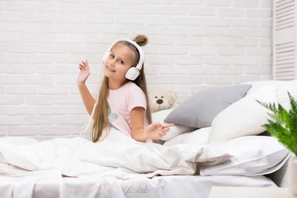 Mała dziewczynka słucha muzyki ze słuchawkami na łóżku. — Zdjęcie stockowe
