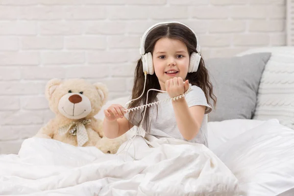 Klein meisje luisteren naar de muziek met de koptelefoon op bed. — Stockfoto