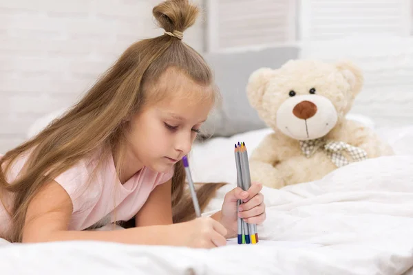 Söt liten flicka ritning bilder medan liggande på sängen — Stockfoto