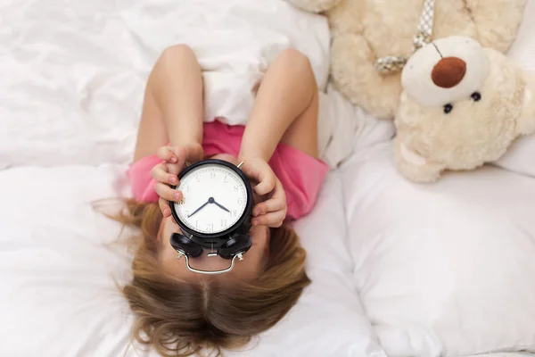 Little girl in pyjamas with clock — Stock Photo, Image