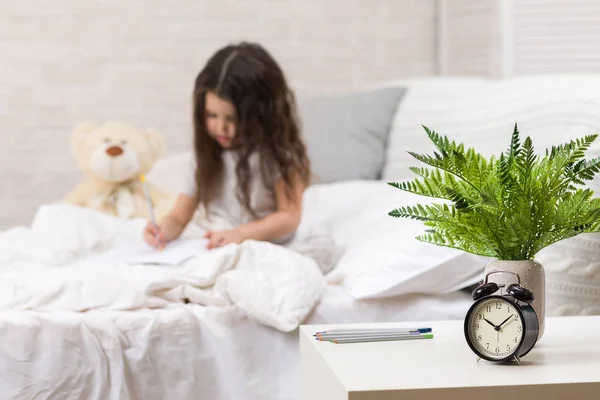 Милая маленькая девочка рисует картинки, лежа на кровати — стоковое фото