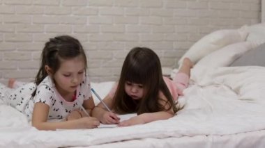 çocuklar yatakta yatarken resim çizer.