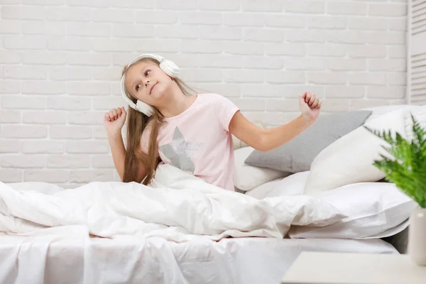 Niña escuchando la música con los auriculares en la cama . — Foto de Stock