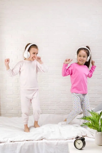 Crianças meninas ouvindo a música com os fones de ouvido e dançando na cama . — Fotografia de Stock