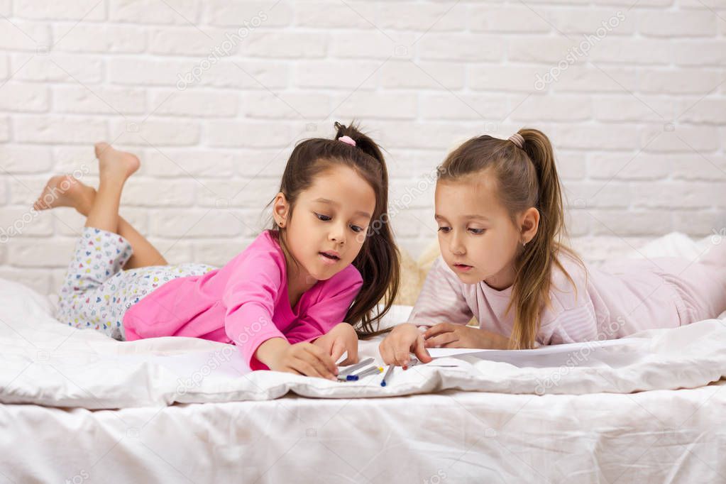kids drawing pictures while lying on bed.